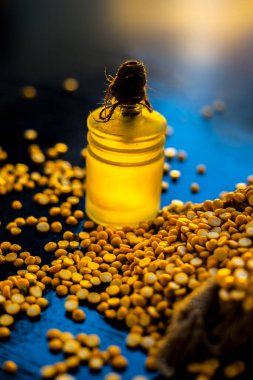 Rafine edilmiş nohut yağını cam bir şişede, parlak, siyah bir ahşap yüzeyde, çiğ sarı mercimek ile kapat..