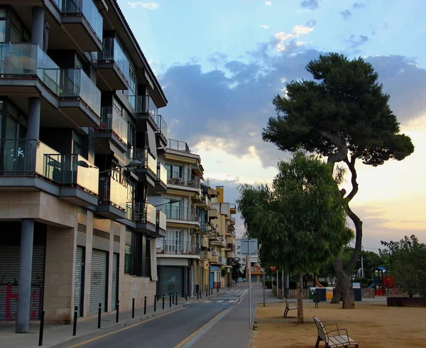 İspanya, Calella, 25 Haziran 2016. İspanyol şehir, otel, cam balkon, güneş parlamayı, uzun boylu ağaç, kum, dar yol, güzel gökyüzü harika şafak