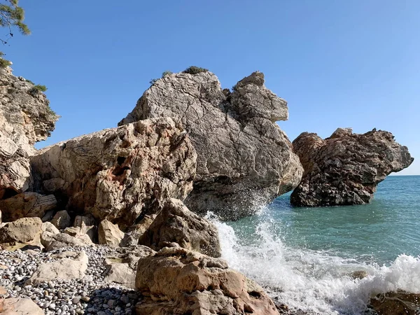 Deniz suyu kıyıdaki büyük kayalara çarpar, bir sürü su sıçratır, deniz, yaz, tatil, güneşli bir gün.