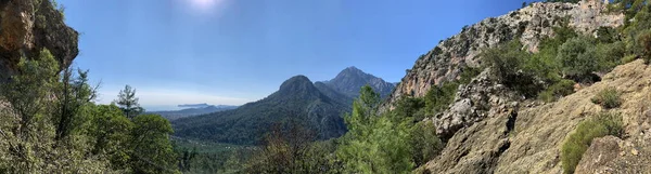 Dağdan diğer dağlara panoramik manzara, yoğun bitki örtüsüyle kaplı iki tepe, deniz kenardan görülebilir, güneşli bir gün, mavi gökyüzü