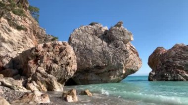 Deniz kıyısının kenarı kayalar ve büyük taşlarla sona erdi, en saf turkuaz su kıyı boyunca sıçrıyor, ses