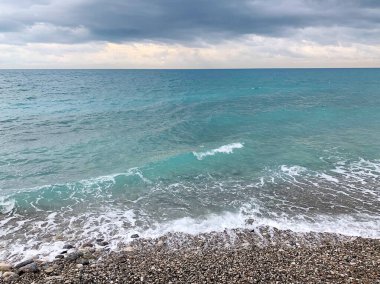 Deniz suyu manzarası, dibe göre farklı renkler, küçük dalgalar, mavi renk, çakıl taşı plajı, kasvetli hava, güzel su rengi.