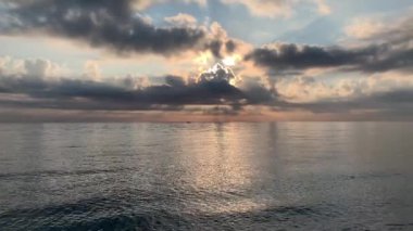 Deniz kıyısında güzel bir gün doğumu, arkasından güneş doğarken bulutlar, güçlü zıt renkler, denizde bir ışık dalgası, suyun sesi, rahatla.