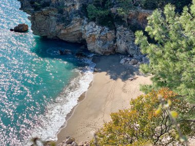 Dağların, kayaların, kumların, deniz dalgalarının arasında harika bir kumsalın yüksekliğinden manzara sürekli sahile gelen rüzgar ağaçları sallıyor, çoğunlukla çam ağaçları, doğayı izlerken bir an rahatlama, denizin sesi, karantinadaki anılar.