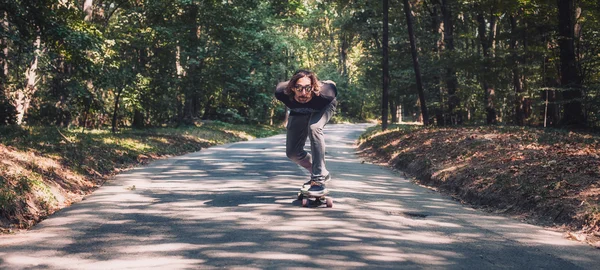 Skater jeździć longboard przez las, panorama — Zdjęcie stockowe