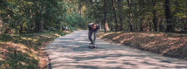 Skateboarder ride a longboard through the forest , panorama — Stock Photo, Image