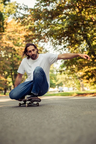 Skateboarder agachamento em um skate e passeio pela floresta — Fotografia de Stock