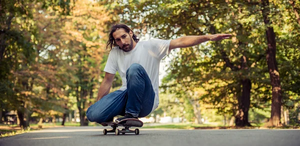 Patinador en cuclillas en un patín y montar a través del bosque —  Fotos de Stock