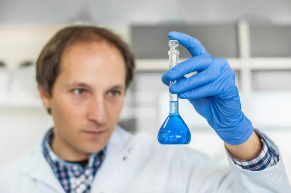 Исследователь мужской лаборатории проводит тесты с голубой жидкостью — стоковое фото