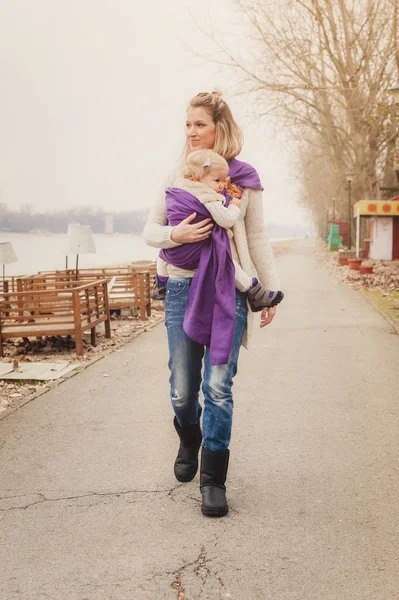 Ung mor med sin lilla dotter i baby carrier halsduk — Stockfoto