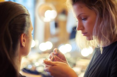 Makeup artist put artificial eyelashes on model clipart