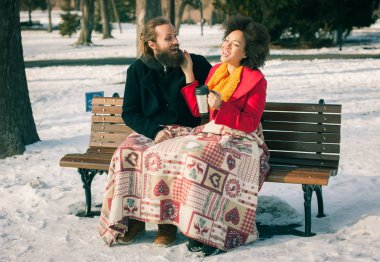 Kışın bankta oturan sıcak içeceklerle seven Çift