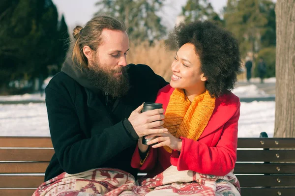 Liebespaar sitzt im Winter mit Heißgetränken auf Bank — Stockfoto