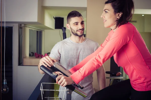 Bisiklete binme egzersiz bisikleti ile onun fitness partne kullanan sportif kadın — Stok fotoğraf