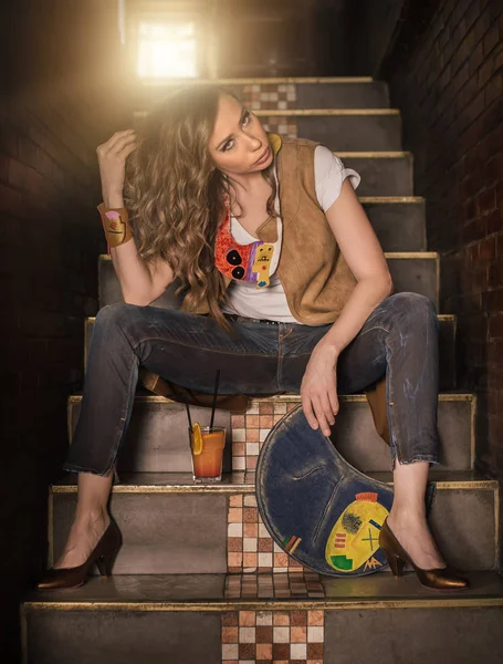 Hermosa mujer de moda en jeans bebiendo cóctel en las escaleras — Foto de Stock