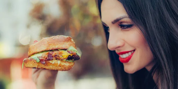 幸せな若い女がおいしいファーストフードのハンバーガーを食べる — ストック写真