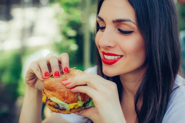 幸せな若い女がおいしいファーストフードのハンバーガーを食べる — ストック写真