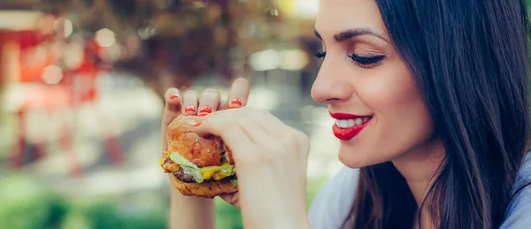 Szczęśliwa młoda kobieta jeść smaczne jedzenie fast burger — Zdjęcie stockowe