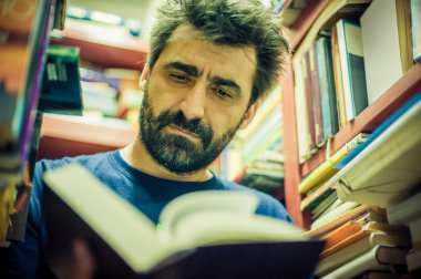 Meraklı adam Kütüphane rafları arasında kitap okuma