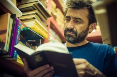 Meraklı adam Kütüphane rafları arasında kitap okuma