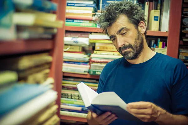 Kíváncsi ember olvasás könyv között a polcokon, a könyvtár — Stock Fotó