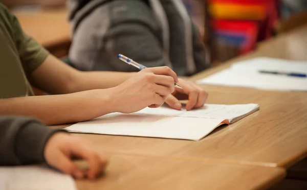 Primo piano delle mani degli studenti sul tavolo della scuola scrivendo sul taccuino — Foto Stock