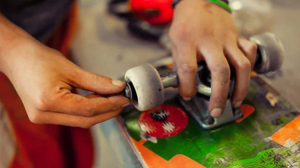 Young man in carpentry workshop fixing wheel on his skateboard — Stock Photo, Image