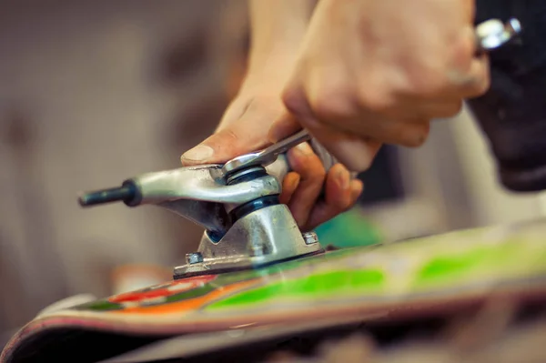 Young man in carpentry workshop fixing wheel on his skateboard — Stock Photo, Image