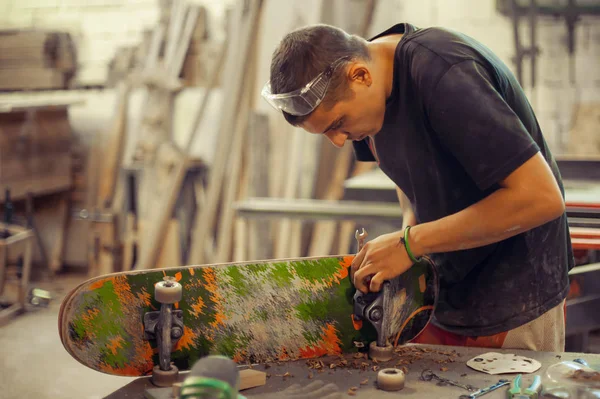 Joven en taller de carpintería fijando rueda en su monopatín —  Fotos de Stock