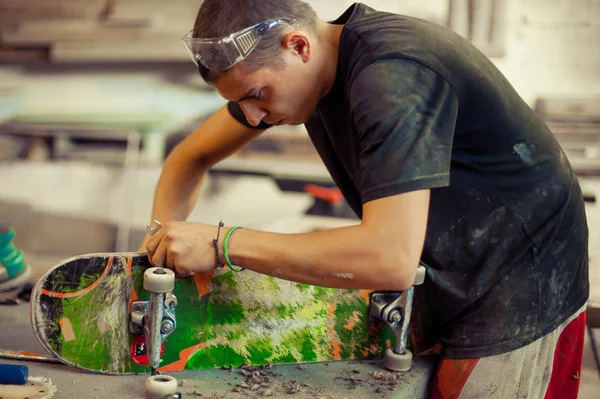 Молодий чоловік у столярній майстерні закріплює колесо на скейтборді — стокове фото