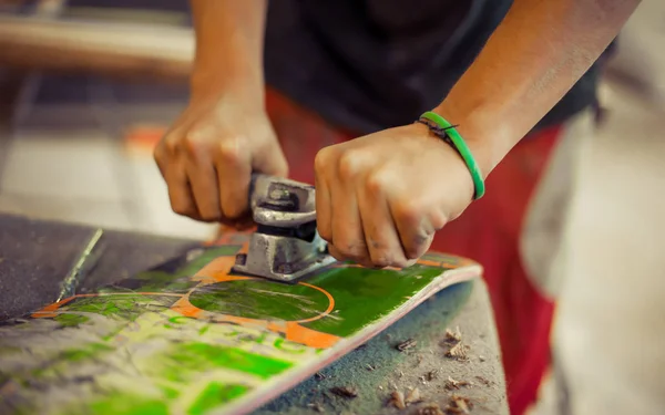 Mladý muž v truhlářské dílně upínání kotouče na jeho skateboard — Stock fotografie