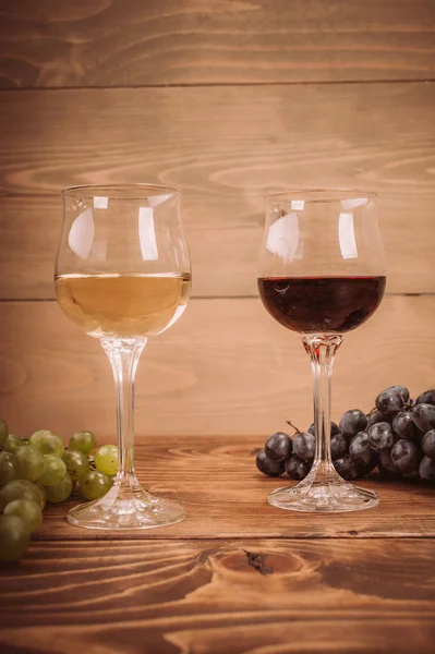 Copas de vino tinto y blanco y uva sobre mesa de madera —  Fotos de Stock