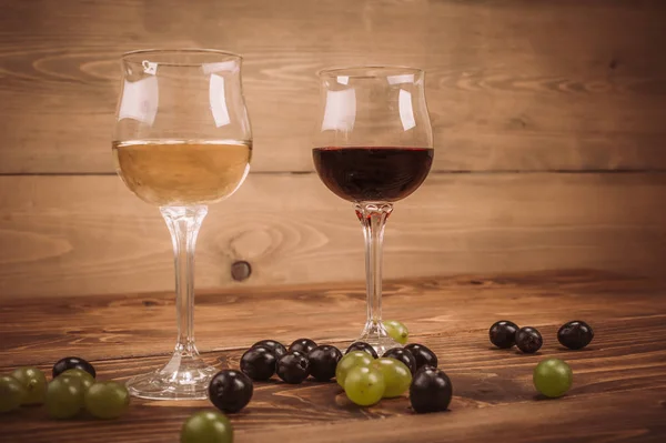 Copas de vino tinto y blanco y uva sobre mesa de madera —  Fotos de Stock