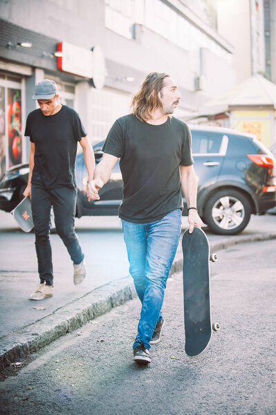 Two pro skateboard rider walking down the street holding skatebo
