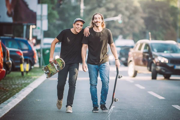 Dois pro skate cavaleiro andando pela rua segurando skatebo — Fotografia de Stock