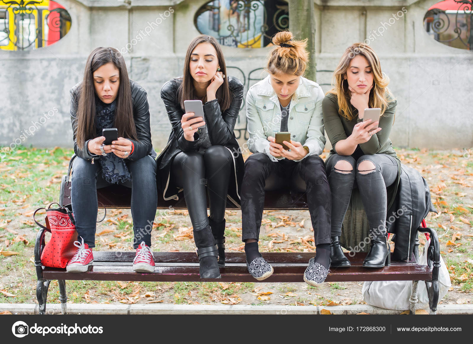 Group Of Girls Using Cellphones On Park Bench Stock Photo