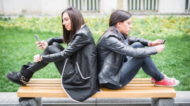 İki kız arkadaş bankta cep telefonu kullanarak