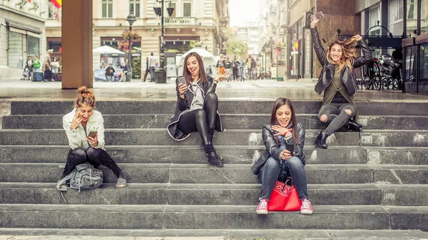 Chica feliz amigos sentados en las escaleras de la ciudad con teléfono inteligente —  Fotos de Stock