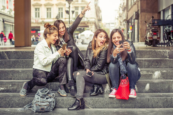 Happy girl friends sitting on the city stairs with smartphone