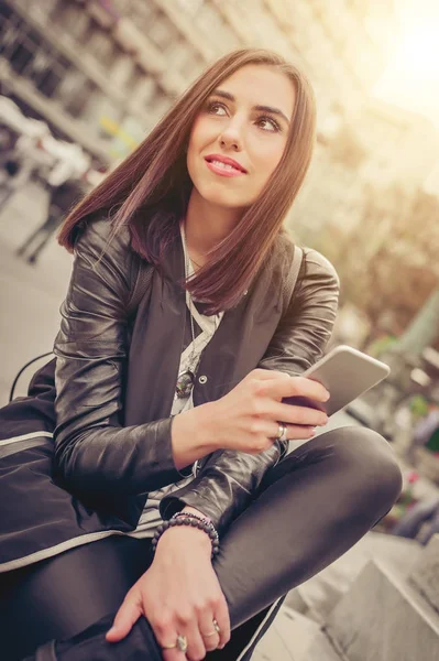Счастливая женщина сидит на улице, печатает сообщения, болтает на умной — стоковое фото