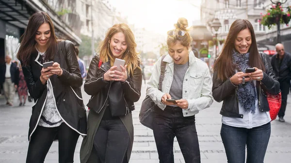 Sokakta yürüyen ve cep telefonu kullanarak mutlu dört arkadaş — Stok fotoğraf