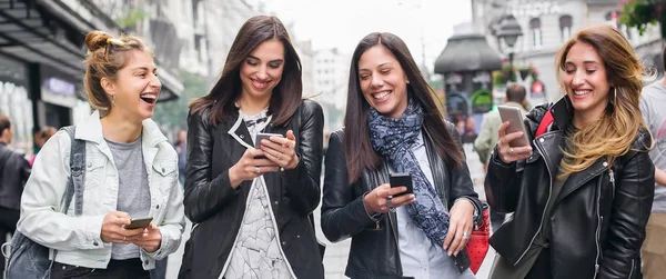 Sokakta yürüyen ve cep telefonu kullanarak mutlu dört arkadaş — Stok fotoğraf