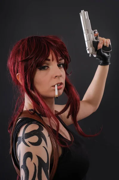 Schöne rothaarige Frau mit Waffe vor dunklem Hintergrund — Stockfoto