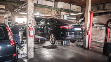 Araba tamircisi hidrolik araba asansörüyle tamirhanede çalışıyor.