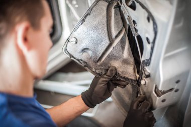 Araba tamircisi bir arabanın kapısında çalışıyor.