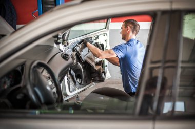 Araba tamircisi bir arabanın kapısında çalışıyor.