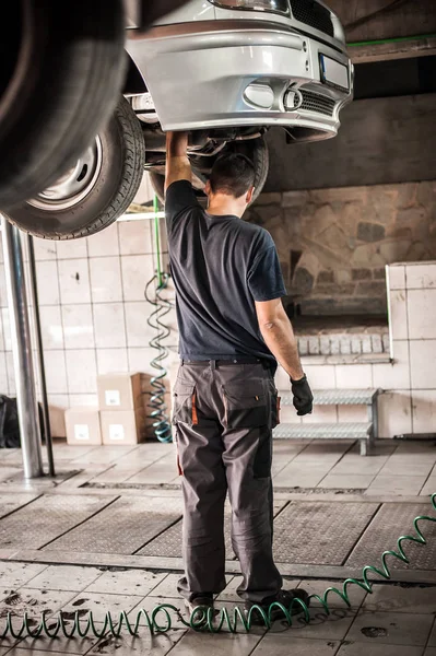 Mecánico de coches trabajando en un garaje de reparación con elevador de coche hidráulico —  Fotos de Stock