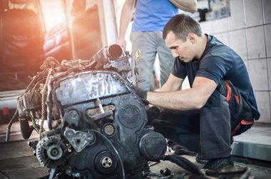 Arabadan çıkarılmış motor. İki otomobil tamircisi araba motorunu tamir eder