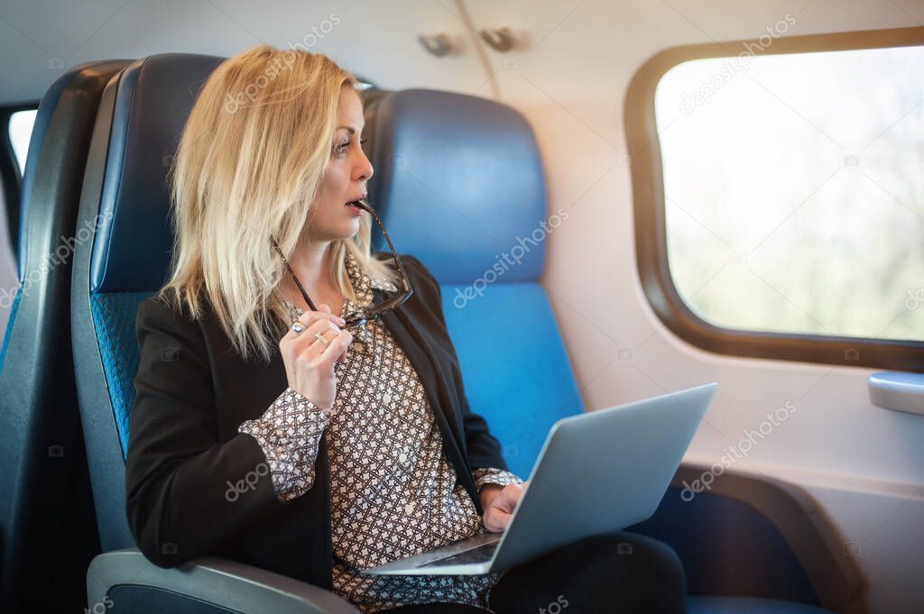 Beautiful woman traveling using laptop in train. Businesswoman pensive looking out the window while working on computer on travel commute to work