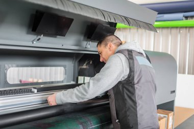 Electrical engineer operator repairs large premium industrial printer and plotter machine in digital printshop office clipart